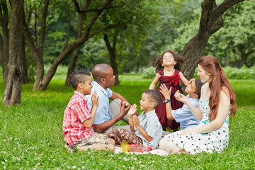 Happy family of six takes rest at picnic in summer park