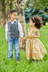 Little girl in beige party frock and boy stand holding hands