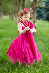 Little girl dressed in bright puffy gown examines big red pencil