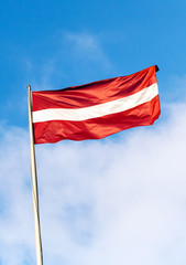 Fototapeta na wymiar Flag of Latvia above blue sky with clouds