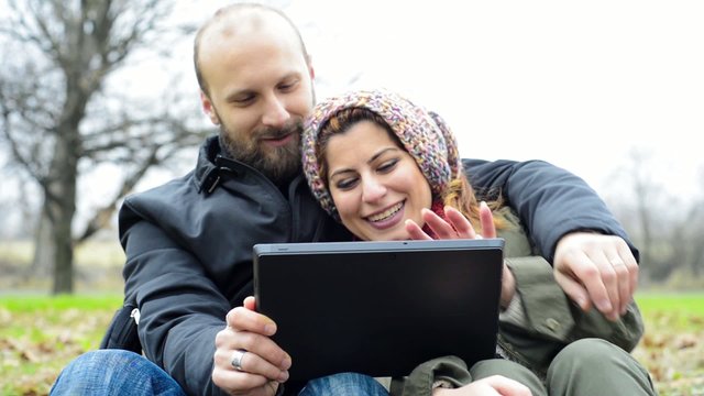 happy lover couple using tablet outdoor in the park winter cold 