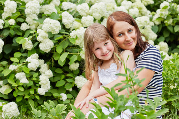 Mother and her little daughter in park among blooming bushes