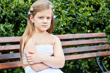 Little girl sits on bench in summer park