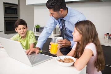 Obraz na płótnie Canvas Father using laptop and kids having breakfast in kitchen