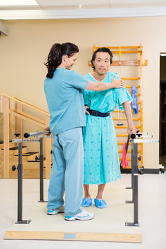 Physical Therapist Assisting Male Patient In Walking
