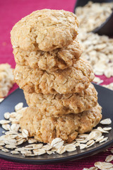 Five oatmeal cookies on red background, scattered oat flakes