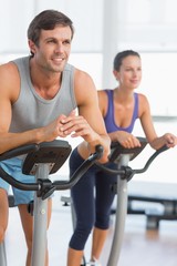 Fototapeta na wymiar Smiling young couple working out at spinning class