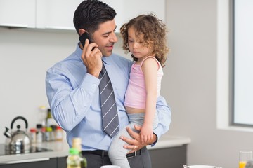 Well dressed father carrying daughter while on call in kitchen
