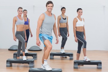 Instructor with fitness class performing step aerobics exercise