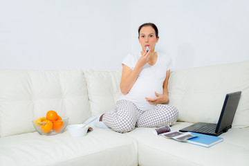 pregnant woman measuring temperature on sofa at home
