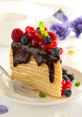 Piece of layer cake with chocolate sauce and berries.