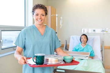 Nurse Holding Breakfast Tray With Patient Lying On Hospital Bed