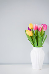 Colorful tulips in white vase on the table on light grey backgro