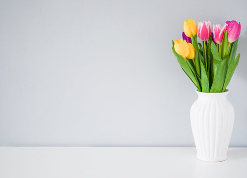 Fototapeta Colorful tulips in white vase on the table on light grey backgro