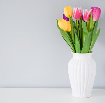 Colorful tulips in white vase on the table on light grey backgro