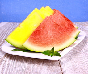 Red and yellow watermelon with mint on white plate