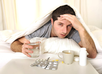 Man with headache and hangover in bed with tablets