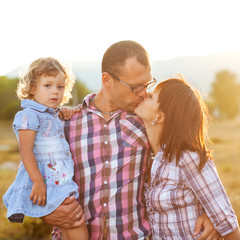 Happy mother, father and daughter in sunset