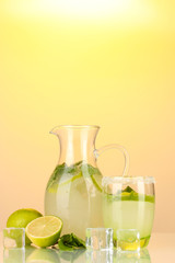 Lemonade in pitcher and glass on yellow background