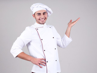 Professional chef in white uniform and hat, on gray background