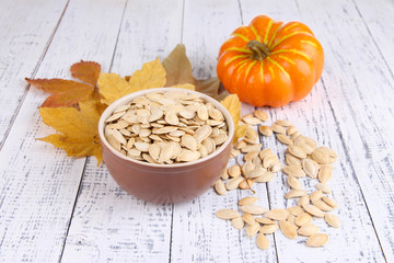 Pumpkin seeds in bowl with pumpkin on wooden background