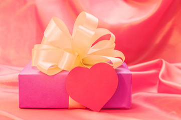 Gift box with yellow bow and red hearts on a silk background