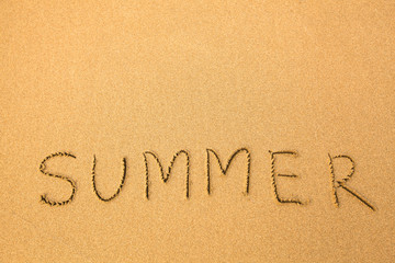 Summer - text written by hand in sand on a beach.