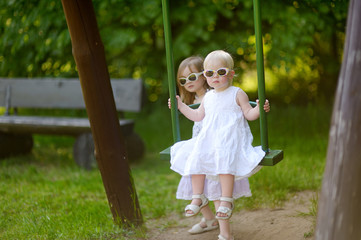 Two sisters having fun on a swing on summer day