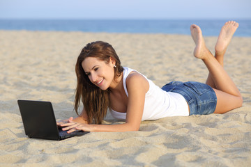 Teenager girl browsing her netbook computer lying on the beach