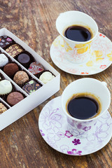Assorted chocolate candies and two cups of coffee on a wooden ta