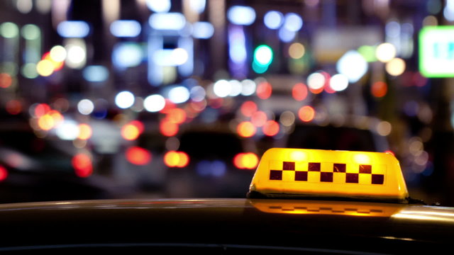 Timelapse of city traffic at night behind taxi sign