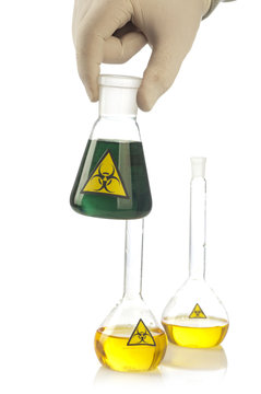 Hand holds glass tube with green fluid and symbol biohazard.