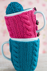 Two blue cups in blue and pink sweater with ball of yarn