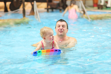 Obraz na płótnie Canvas Father teaching his daughter to swim with floating board