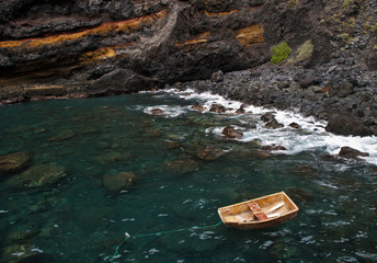 small wooden boat anchored near rocks