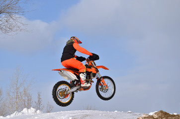 MX rider on the bike jumps from a hill on a snowy highway