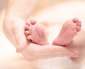 Obraz na płótnie Canvas Tiny Newborn Baby's feet on female hands closeup.