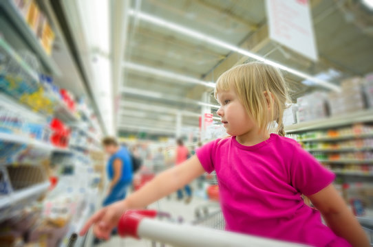 Adorable girl at shopping cart select products in supermarket