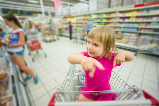 Adorable girl at shopping cart select products in supermarket