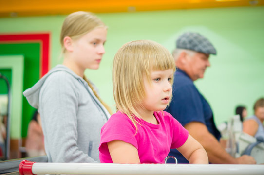 Adorable girl at shopping cart and mother stay in queue at cash