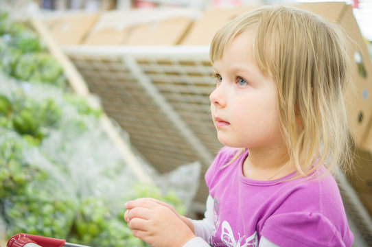 Adorable girl at shopping cart select fruits in supermarket