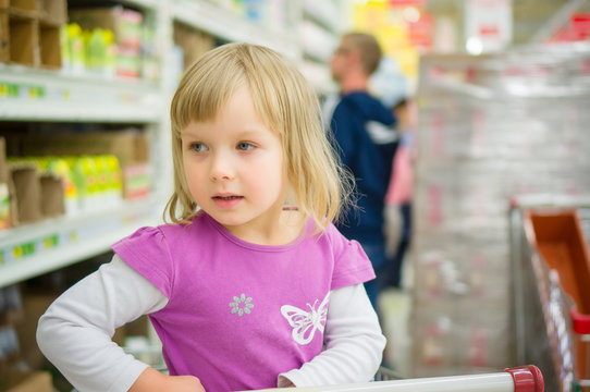 Adorable girl at shoppoing cart grimacing in supermarket