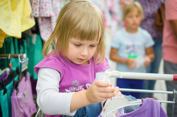 Obraz premium Adorable girl at shopping cart select clothes in supermarket