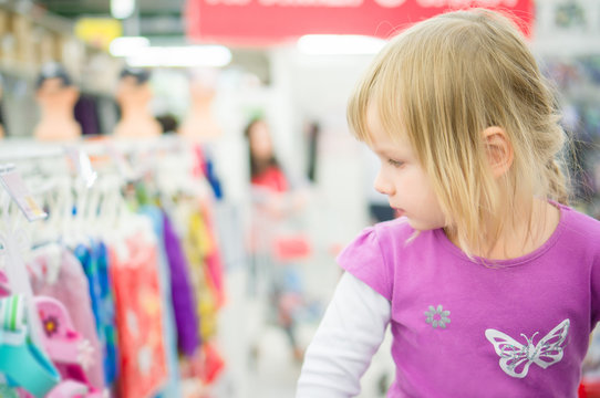 Adorable girl at shopping cart select clothes in supermarket