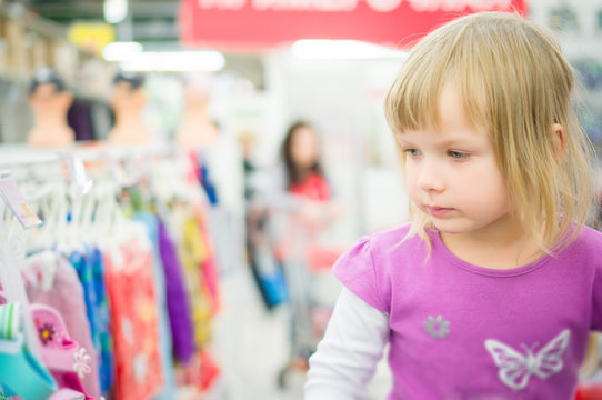 Adorable girl at shopping cart select clothes in supermarket