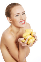 Beautiful naked caucasian woman is holding fresh, raw potatoes.