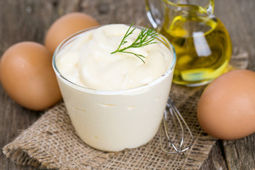 Mayonnaise in bowl with egg and olive oil on an old wooden table