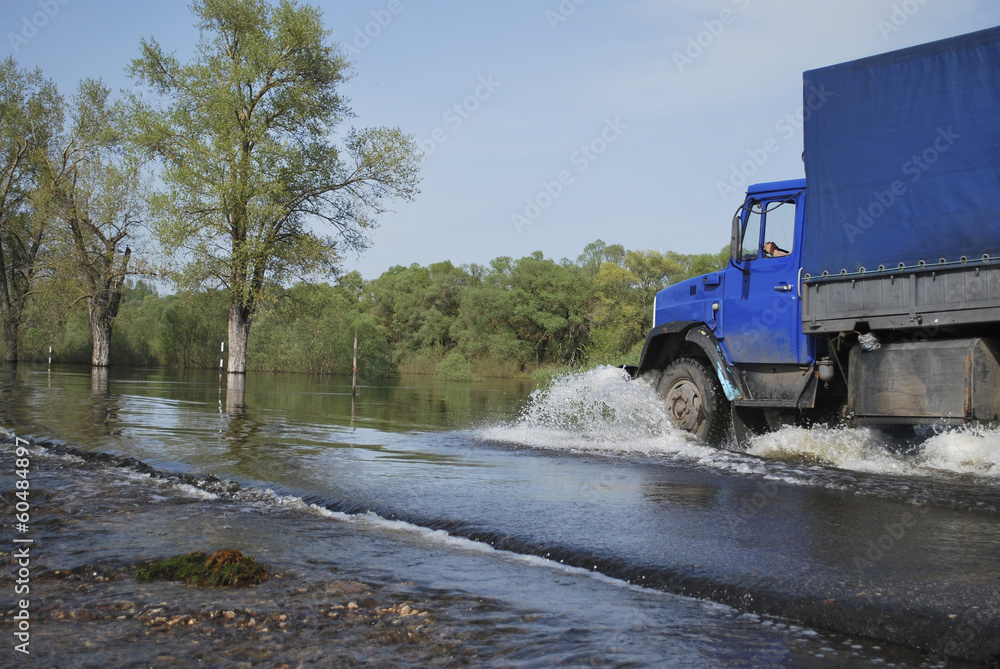 Wall mural truck travels across the river which came out of its banks and f