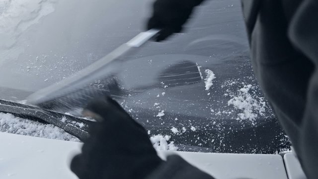 winter driving - woman sweeping snow from a windshield