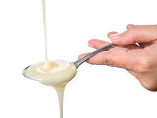 Female hand with a spoon pouring condensed milk